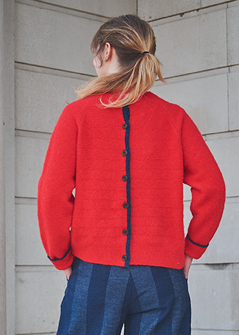 Person wearing a red cardigan with black buttons against a light gray wall.