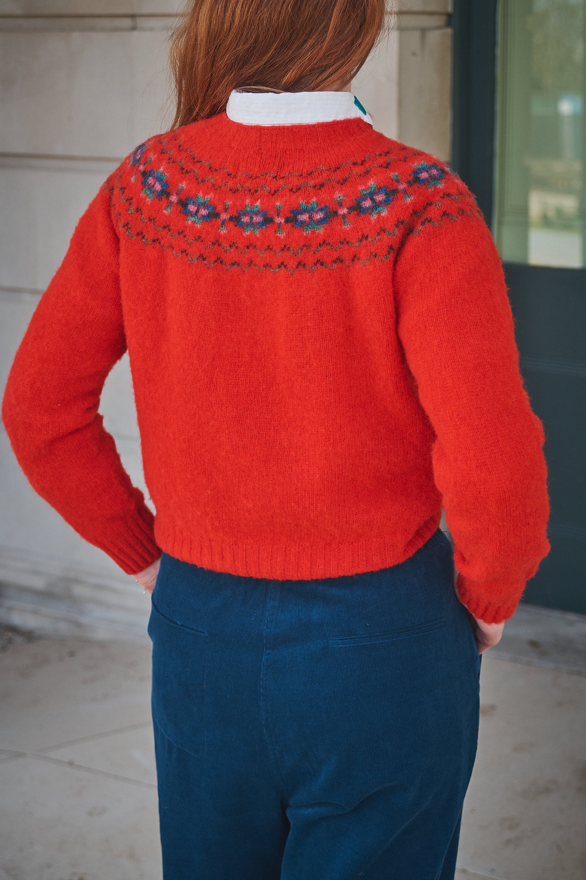 Person wearing a red sweater with a patterned yoke, standing against a neutral background.