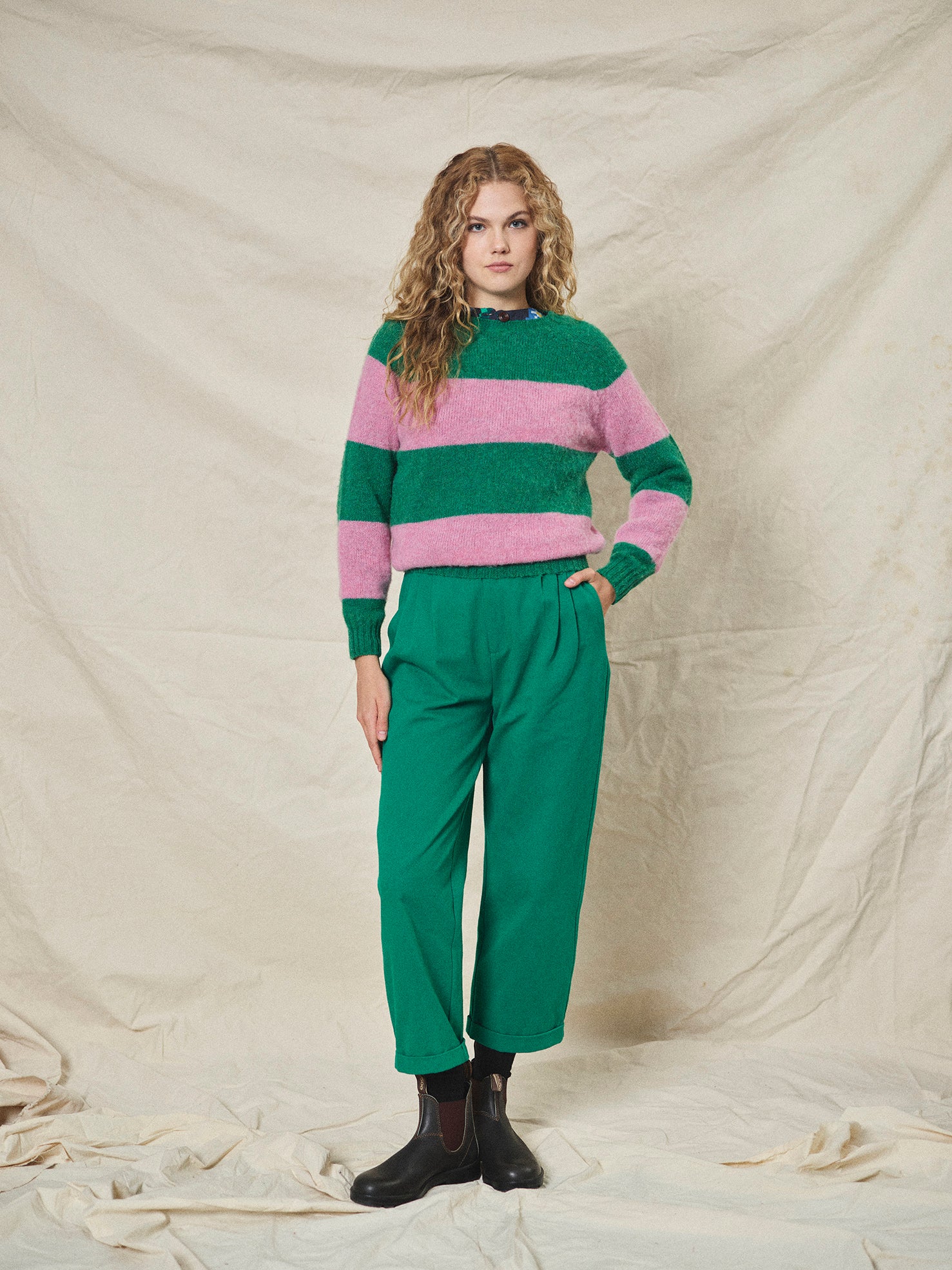Woman wearing a green and pink striped sweater with green pants against a beige background