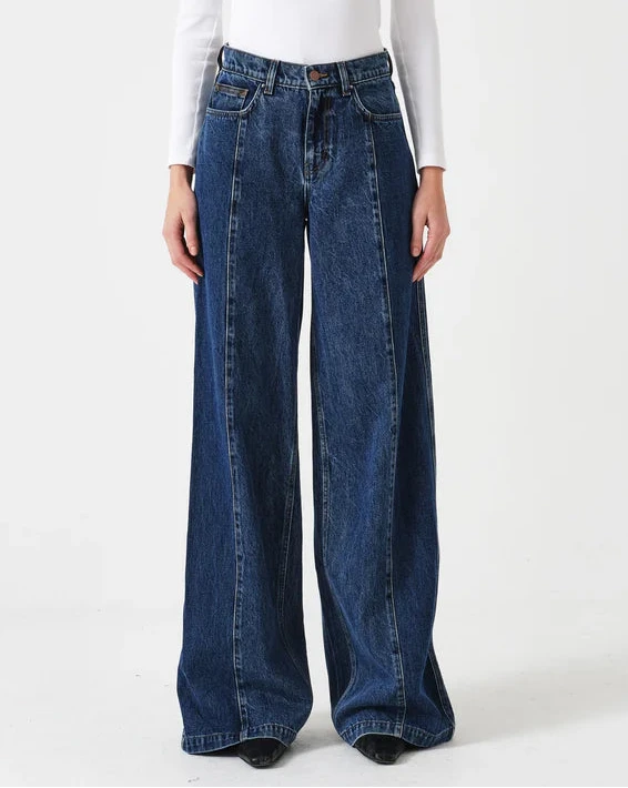 Woman wearing a white long-sleeve top and blue wide-leg jeans on a white background