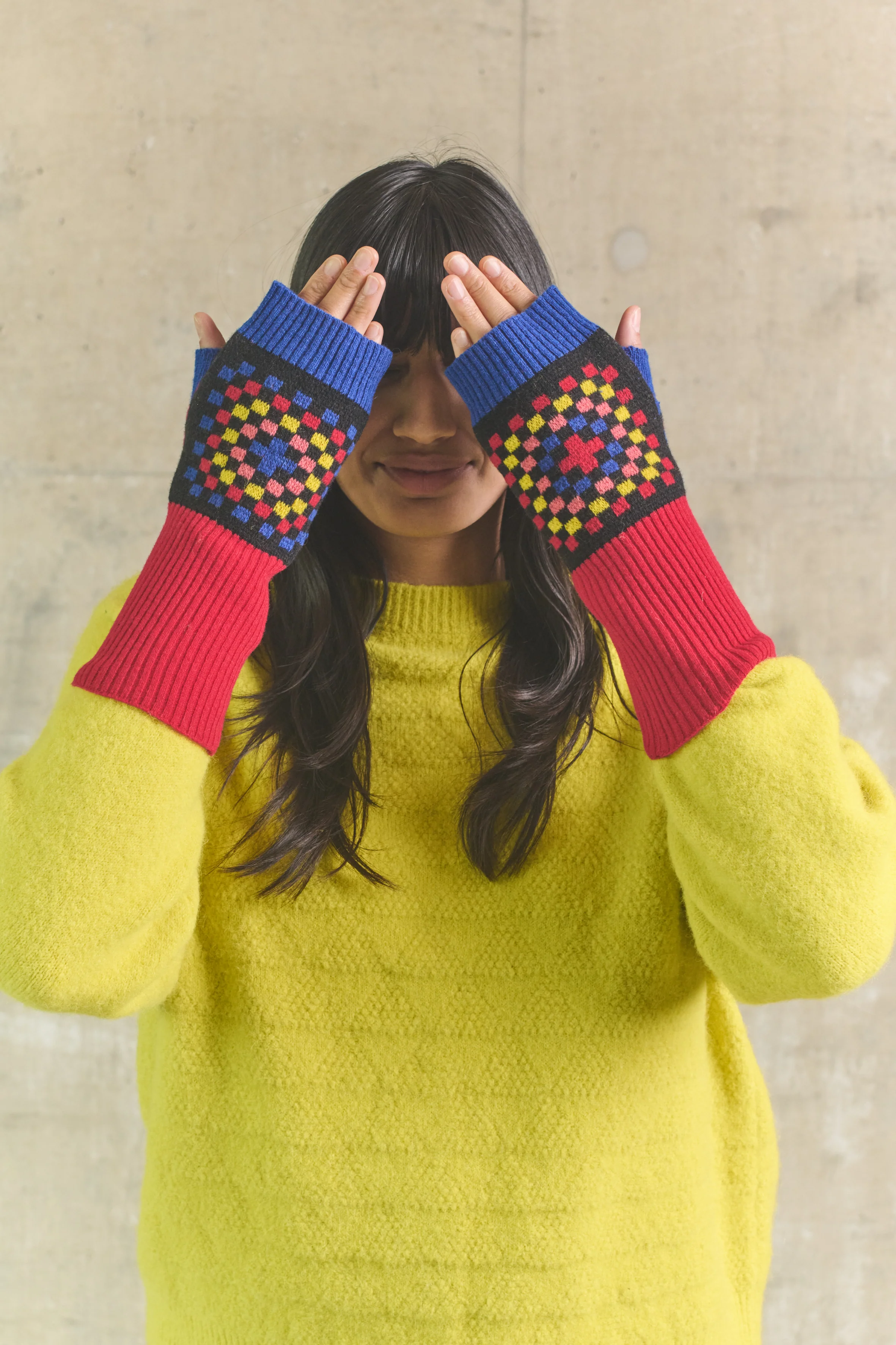 Person wearing colorful fingerless gloves with a geometric pattern against a plain background