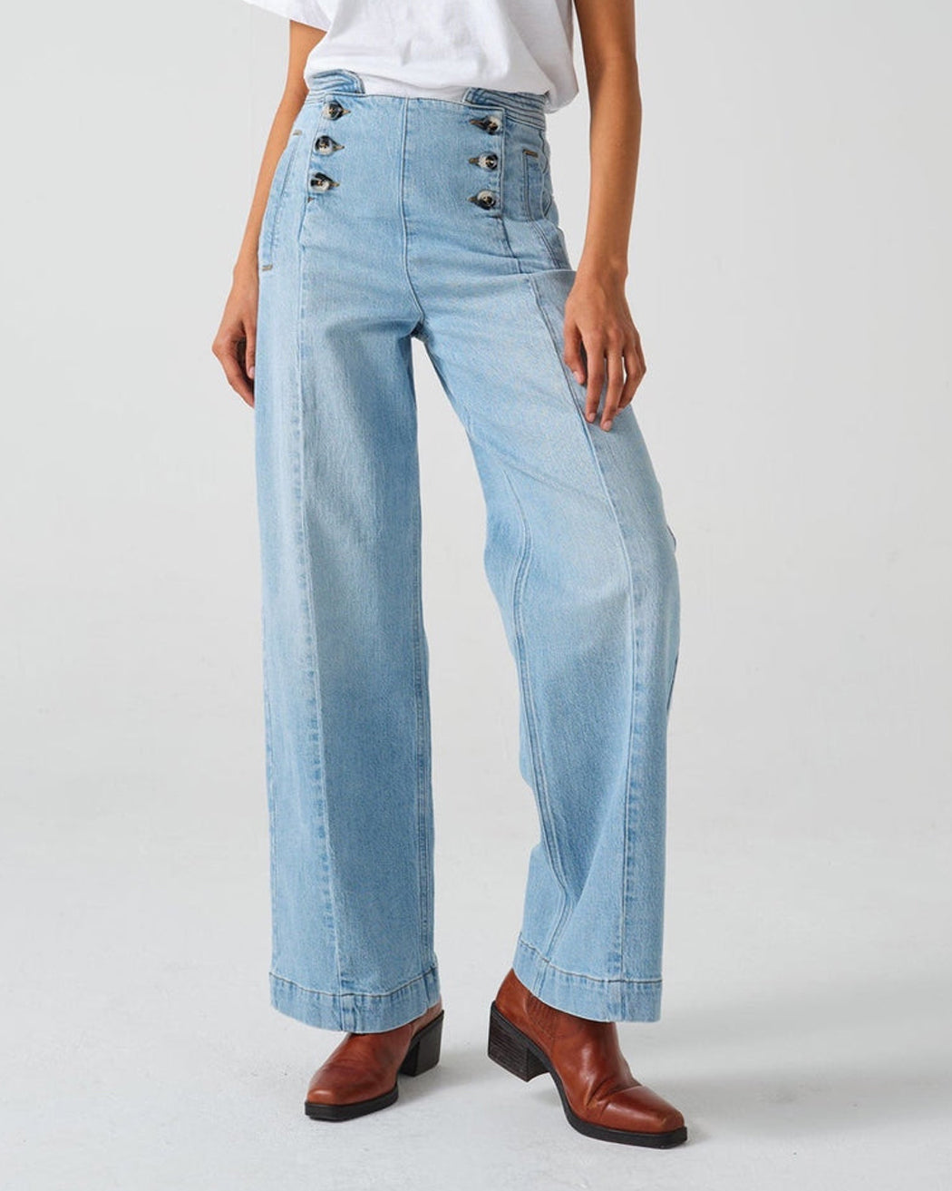A pair of high-waisted, wide leg jeans with a button-up front in an oceanic blue wash. The jeans are worn with brown ankle boots.
