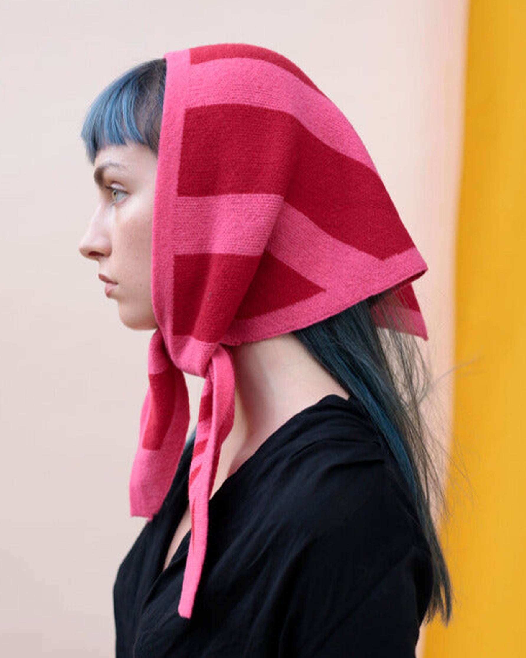 Person wearing a pink and red patterned headscarf against a beige and yellow background