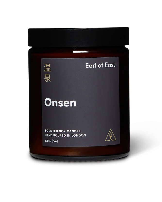 A hand-poured soy wax candle in an amber glass jar with a black label reading 'EARL OF EAST ONSEN'