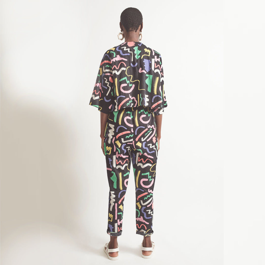 A pair of black holiday trousers with a multicolored scribble print, featuring a high waist, tapered leg, and side pockets.